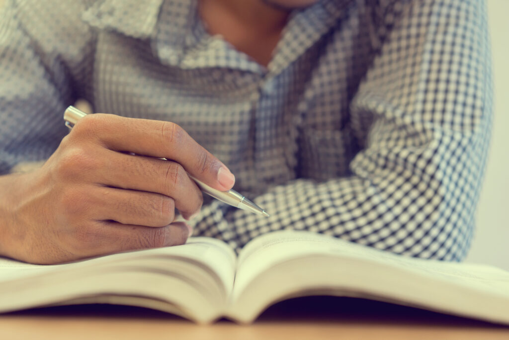 close up student man hand holding pen for guideline reading on text book at campus library for examination education concept